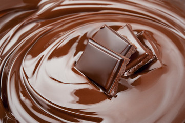 Melted pieces of chocolate bar in glossy chocolate splash background. Front view.