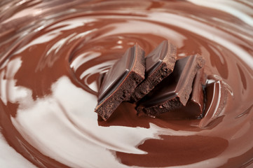 Melted pieces of chocolate bar in glossy chocolate splash background.