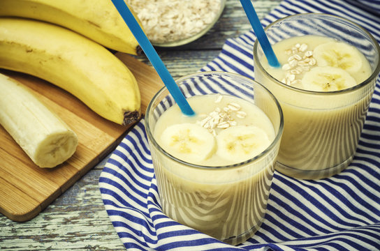 Banana smoothie.  Milkshake with banana and oatmeal. Two glasses of cocktail with a straw of blue color. Nutritious, healthy and tasty breakfast