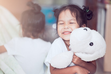 Happy asian child girl smiling and hugging her doll with love in the house in vintage color tone