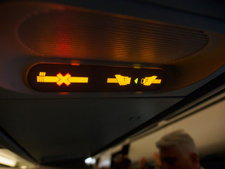 Close-up detail of the no smoking symbol illuminated yellow on an airplane, with people standing in the background. Frankfurt International Airport, Germany. Travel and aircraft concept. - 168826984
