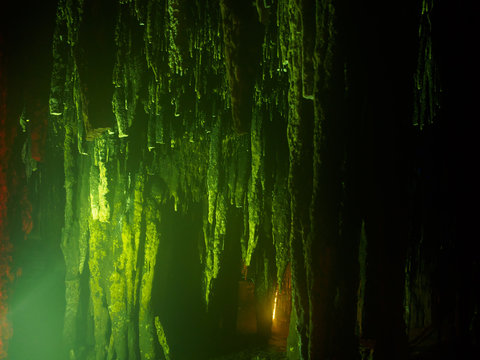 Wide angle view of multiple long stalacites and columns hanging from the ceiling of a cave, lit by an eerie green glow. Khao Bin Cavern, Ratchaburi, Thailand. Travel and environment concept.