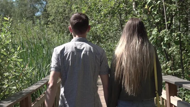 Beautiful couple of lovers walking on a wooden bridge holding hands close-up 4k.