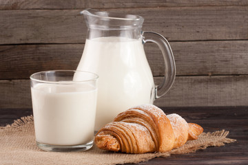 jug and glass of milk with croissant on a wooden background
