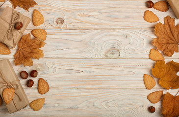 Flat lay frame of yellow leaves, cookies in the form of leaves, hazelnuts and gift boxes on a light wooden background.