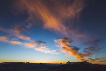 Naklejka na ściany i meble Amazing colorful sunset high in mountains. Orange clouds and blue sky