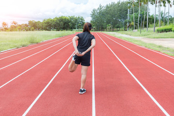 Fototapeta premium Young woman runner stretching legs before run during sunny morning on stadium track