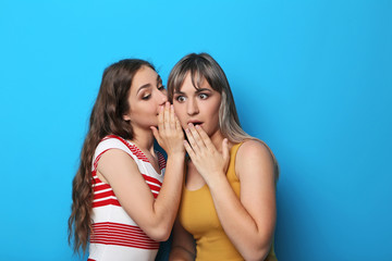 Two young woman whispering a secret on blue background