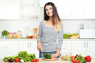 Beautiful young woman cooking salad in the kitchen