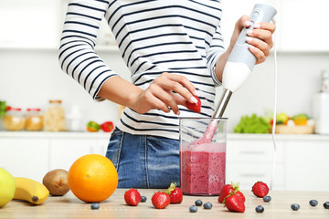 Young woman cooking smoothie in blender