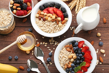 Oat flakes in plate with berries, nuts, honey and milk on wooden table