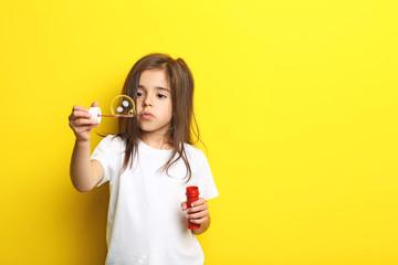 Beautiful little girl blowing soap bubbles on yellow background
