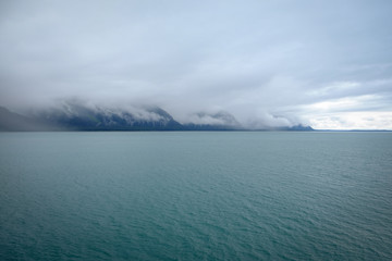 Fototapeta premium Sun breaking through cloud covered mountains overlooking a green ocean