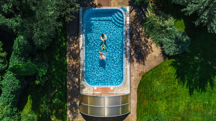 Aerial top view of family in swimming pool from above, happy mother and kids swim on inflatable ring donuts and have fun in water on family vacation
