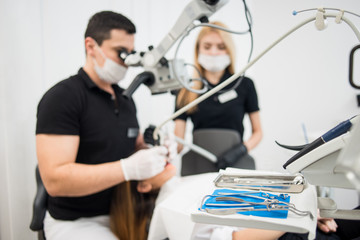 Male dentist and female assistant treating patient teeth with microscope at dental clinic office. Focus on the dental tools. Medicine, dentistry and health care concept. Dental equipment