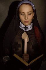 Beautiful nun with a candle reading the Bible. religious concept