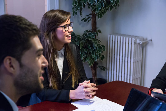 Group of young people sitting at table in office posing with various gadgets and communicating cheerfully. 