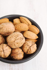 walnuts and almond on black bowl on wooden background