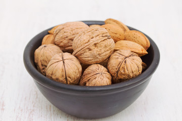 walnuts and almond on black bowl on wooden background