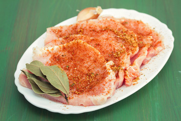 raw pork with herbs on white dish on wooden background