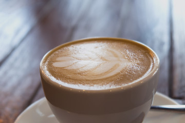close up of a cup of coffee latte on wooden table in coffee shop.
