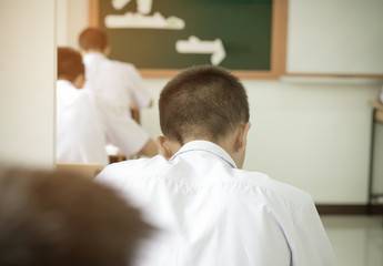 Asian boy students sittingl on wood desk with Exams paper sheet or test paper in class room, education concept