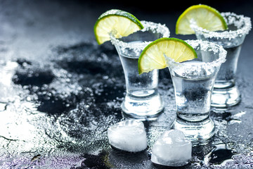 Tequila shot with lime slices and salt on dark background