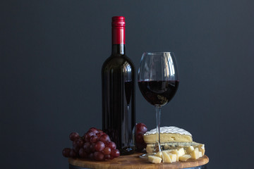 Bottle and glass with red wine near cheese composition on a wooden board