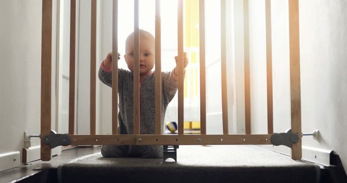 child playing behind safety gates in front of stairs at home
