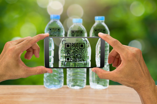Man's hands holding smartphone scanning QR code on drinking water bottle in the garden, business concept