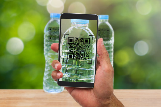 Man's hands holding smartphone scanning QR code on drinking water bottle in the garden, business concept