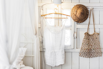 Interior of light modern wooden house inside, vintage window with shutters and decorative curtains. Straw hat, hanging dress and handmade wicker bag. Rustic and village style © Oleg Breslavtsev