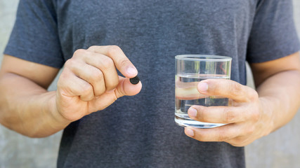 Man holding an activated charcoal pills and a glass of water.