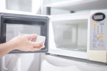 woman hand using are bringing food into the microwave oven at home. To reheat frozen food for their...
