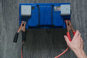 The male hand connects the terminals to the car's batteries on a wooden background