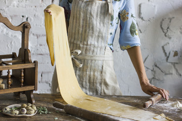 Young woman in apron holding a dough for homemade pasta at rustic kitchen