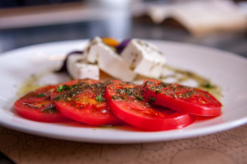 Mozzarella with tomatoes, italian herbs and rucola on a white plate on a wooden table in restaurant, closeup