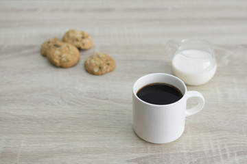 COFFEE MUG AND COOKIES
White coffee mug with milk jar and a group of oat meal raisin cookies on the wood table. 