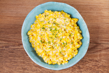Creamy corn in bowl on wooden background. Skillet sweet corn. Homemade corn dish. View from above, top studio shot