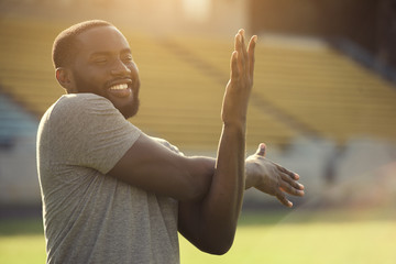 A handsome black man is performing stretching exersises for his arms in the field