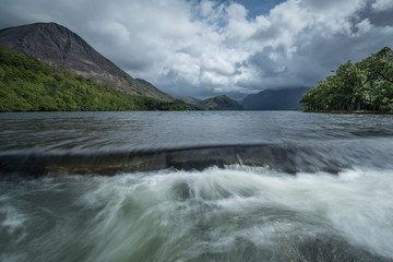 The view of Crummock water with the weir in the foreground and blue cloudy sky in the background.