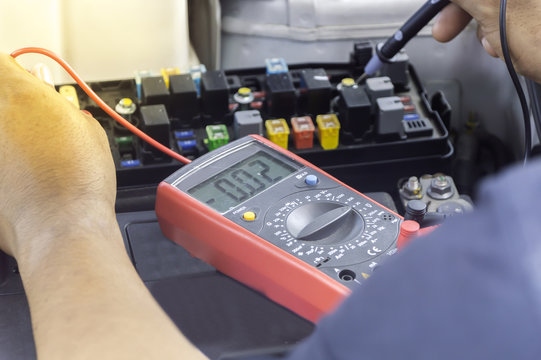 Auto mechanic uses a multimeter voltmeter to check the voltage level in a car.