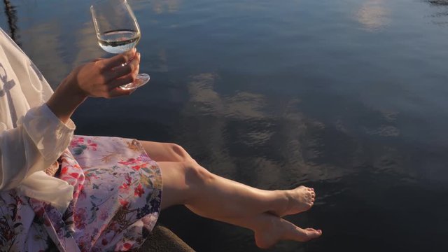 Pretty young woman outdoors drinking wine on embankment of the river
