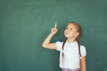 Smiling young little child girl in school on blackboard background. Education and school concept