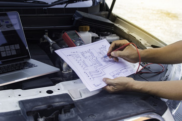 Auto mechanic uses a multimeter voltmeter to check the voltage level in a car batter.