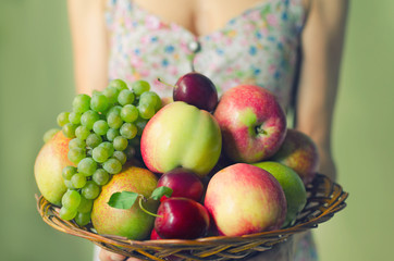 A large wooden plate with ripe fruits in the hands of a young woman. Harvest concept