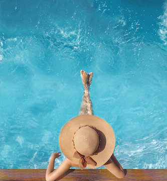 Top view of woman in straw hat relaxing in swimming pool at luxury villa resort. Summer holiday idyllic background. Vacations Concept. Exotic Paradise.