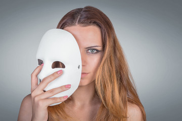 Young emotional woman holding mask in a hands pose in studio on gray background