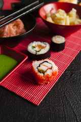 Fototapeta na wymiar Sushi rolls, ginger and wasabi on red mat and black table