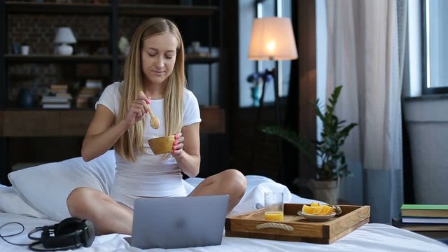 Cheerful woman eating healthy breakfast in bed